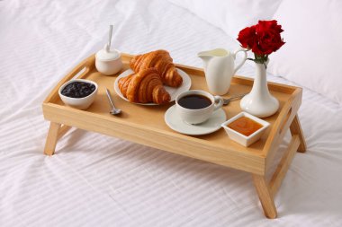 Yatakta servis edilen lezzetli kahvaltı. Taze kruvasan, kahve, reçel ve bal tahta tepside.