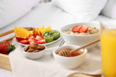 Yatakta servis edilen lezzetli kahvaltı. Yulaf ezmesi, meyve suyu, meyve, badem ve bal tepside, yakın plan.