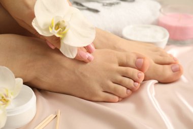 Pedikür sonrası ipek kumaş üzerinde düzgün ayak tırnakları olan kadın, yakın plan.