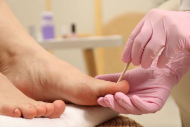 Güzellik salonunda müşterinin ayak tırnaklarıyla çalışan profesyonel pedikür uzmanı.