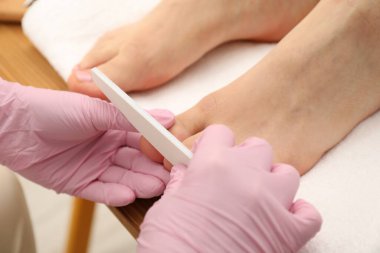 Profesyonel pedikür uzmanı müşterisinin ayak tırnaklarını güzellik salonunda törpülüyor.