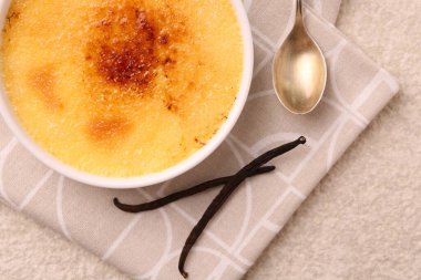 Lezzetli creme brulee kasede, vanilya kabukları ve kaşık açık dokulu masa, üst manzara