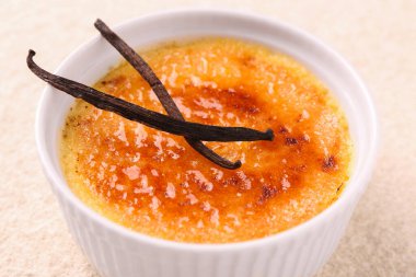 Lezzetli creme brulee ve vanilyalı kaplar açık renkli masada, yakın plan.