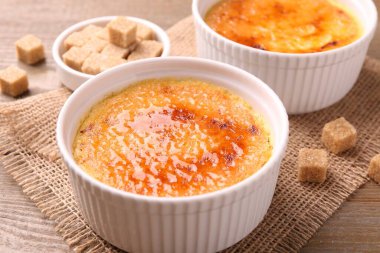 Lezzetli creme brulee kaseler ve şeker küpleri ahşap masa, yakın çekim