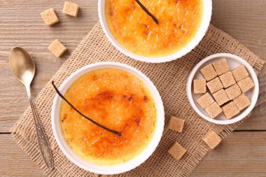 Lezzetli creme brulee kaseler, vanilya kabukları ve şeker küpleri ahşap masa, üst görünüm
