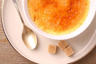 Lezzetli creme brulee kasede, şeker küpleri ve kaşık ahşap masada, üst manzara