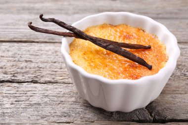Lezzetli creme brulee kasede ve ahşap masada vanilya kabukları, yakın plan