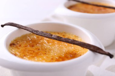 Lezzetli creme brulee kasede ve vanilya kapsülü masada, yakın plan