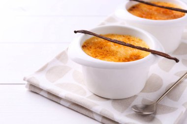 Lezzetli creme brulee kaseler, vanilya kapsülleri ve beyaz ahşap masa üzerinde kaşık, yakın çekim