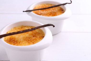 Lezzetli creme brulee kaseler ve beyaz ahşap masa üzerinde vanilya kabukları, yakın çekim