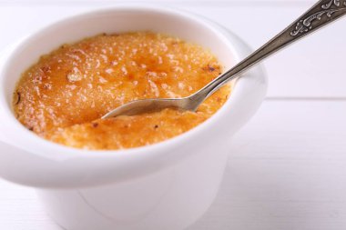 Beyaz ahşap masadaki kaseden kaşıkla leziz creme brulee alıp yakın plan çekiyoruz.