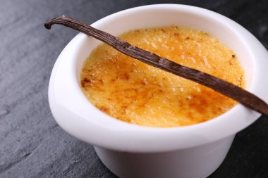 Lezzetli creme brulee kasede ve koyu gri desenli masada vanilya kabuğu