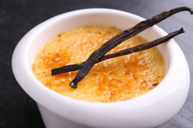 Lezzetli creme brulee kasede ve koyu gri masada vanilya kabukları, yakın plan