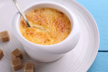 Açık mavi ahşap masada servis edilen kasedeki leziz creme brulee, yakın plan.