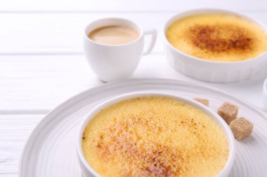 Lezzetli creme brulee kaseler, şeker küpleri ve beyaz ahşap masa üzerinde kahve, yakın çekim