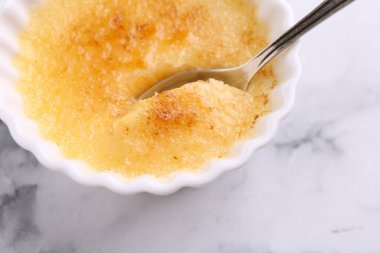 Lezzetli creme brulee kasede ve kaşıkla beyaz mermer masada, üst manzara