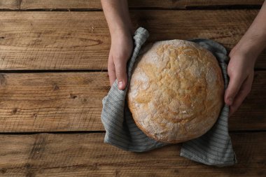 Ahşap masada bir somun taze ekmek tutan adam, üst manzara. Metin için boşluk