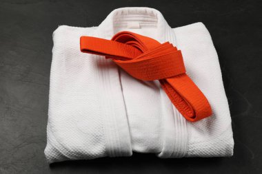 Orange karate belt and white kimono on gray background clipart