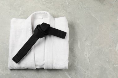 Black karate belt and white kimono on gray marble background, top view. Space for text clipart