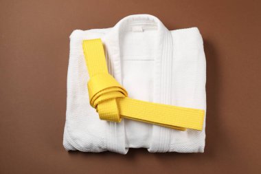 Yellow karate belt and white kimono on brown background, top view clipart