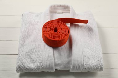 Orange karate belt and white kimono on wooden background clipart