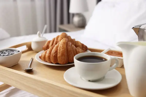 Wooden tray with tasty breakfast on bed at home, closeup