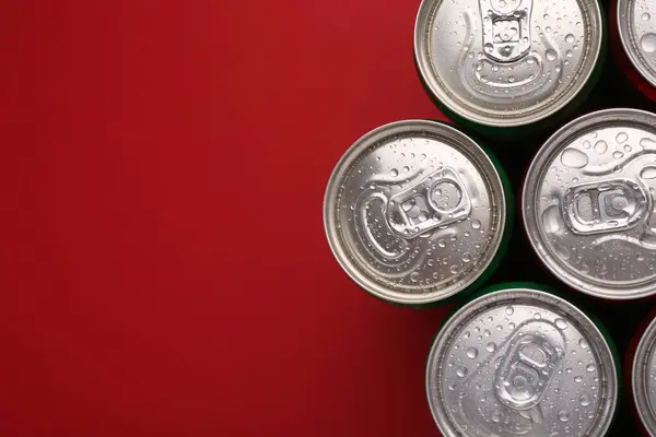 Energy drinks in wet cans on red background, top view. Space for text