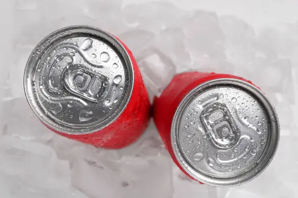 Energy drinks in wet cans on ice cubes, flat lay