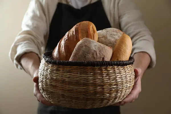 Man holding wicker basket with different types of bread on beige background, closeup