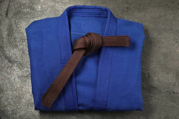 stock image Brown karate belt and blue kimono on gray background, top view