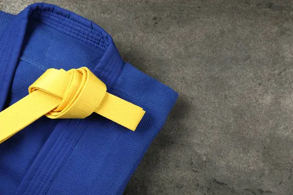 stock image Yellow karate belt and blue kimono on gray textured background, top view. Space for text