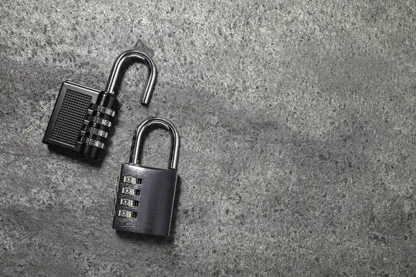 Steel combination padlocks on grey table, top view. Space for text