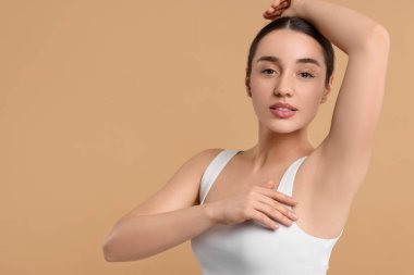 Güzel bir kadın bej arka planda pürüzsüz ciltli koltukaltını gösteriyor.