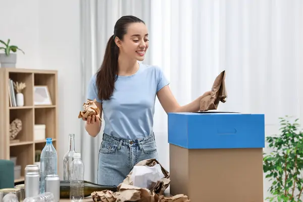 Garbage sorting. Smiling woman throwing crumpled paper into cardboard box in room