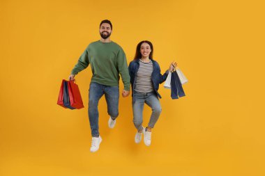 Alışveriş torbalarıyla turuncu arka planda zıplayan mutlu çift.