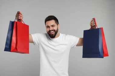 Gri arka planda bir sürü kağıt torbası olan mutlu bir adam.
