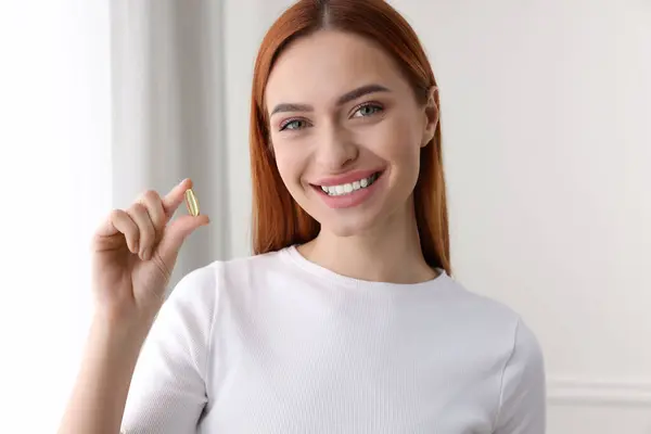 Beautiful young woman with vitamin pill at home