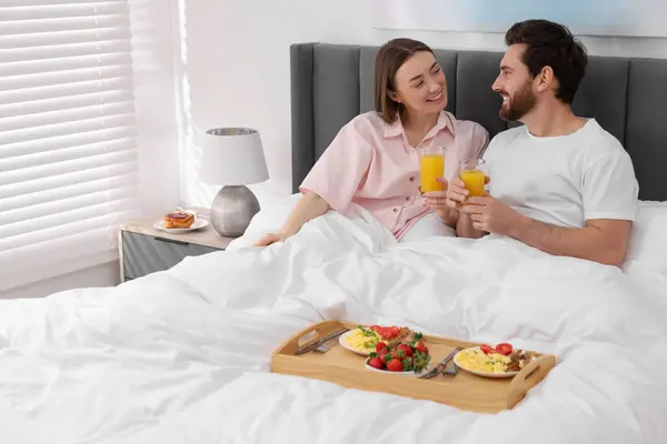 Happy couple eating tasty breakfast in bed at home. Space for text