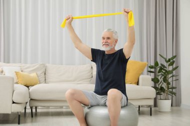 Son sınıf öğrencisi evde spor salonunda elastik direniş bandıyla egzersiz yapıyor.