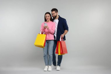 Alışveriş torbaları ve gri arka planda akıllı telefonları olan mutlu çift.
