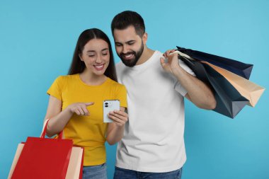 Alışveriş torbaları ve açık mavi arka planda akıllı telefonları olan mutlu çift.