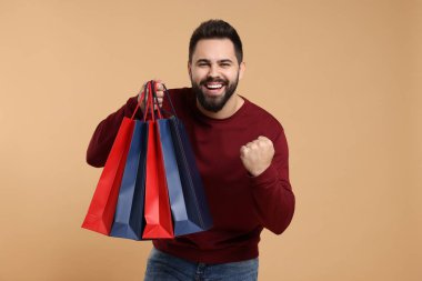 Bej arka planda bir sürü kağıt alışveriş torbası olan mutlu bir adam.
