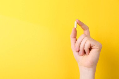 Sarı arka planda vitamin kapsülü tutan kadın, yakın plan. Metin için boşluk