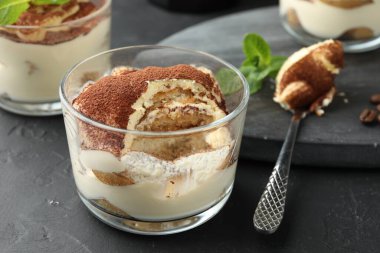 Gözlüklü lezzetli tiramisu ve siyah masada kaşık, yakın plan.