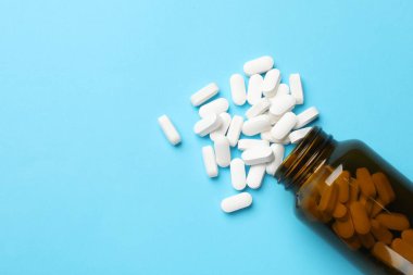 Açık mavi arka planda şişe ve vitamin kapsülleri, üst manzara. Metin için boşluk