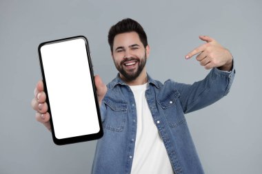 Gri arka planda boş ekranı olan akıllı telefonu tutan mutlu adam.