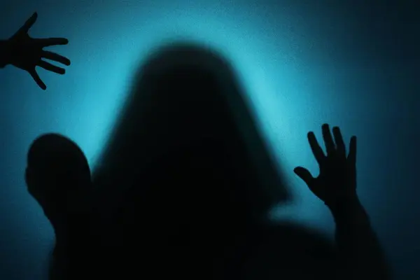 Silhouette of ghosts behind glass against blue background