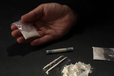 Uyuşturucu bağımlılığı. Kokain ve dolar banknotlu bir adam karanlık masada, yakın plan.