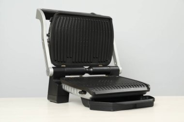 Beyaz ahşap masada gri arka planda elektrikli ızgara. Yemek pişirme aygıtı