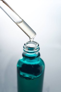 Açık gri arka planda pipetten şişeye damlatan nemlendirici serum, yakın plan.